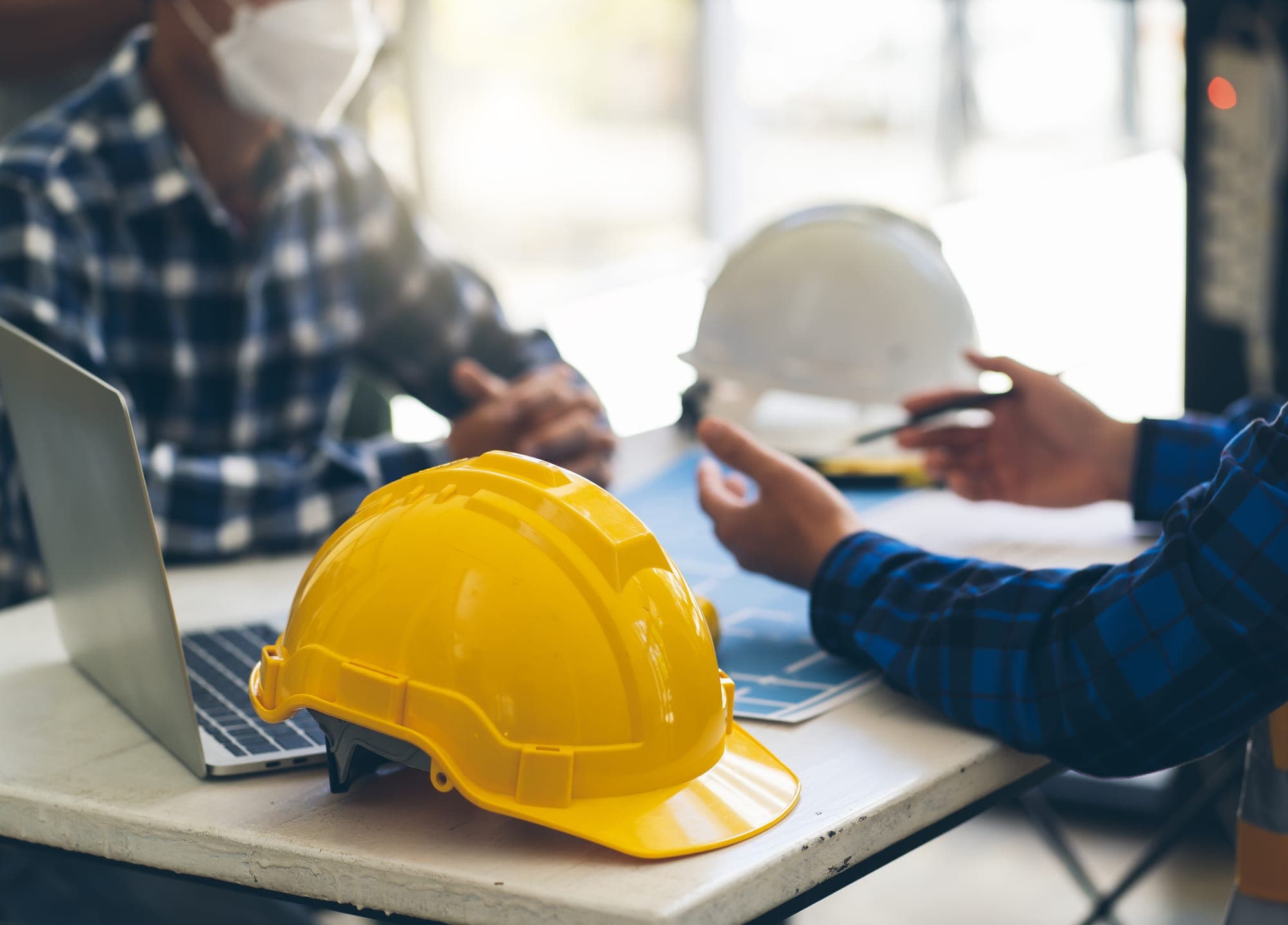 Casque de chantier jaune posé devant un ordinateur portable, pendant une réunion sur plans