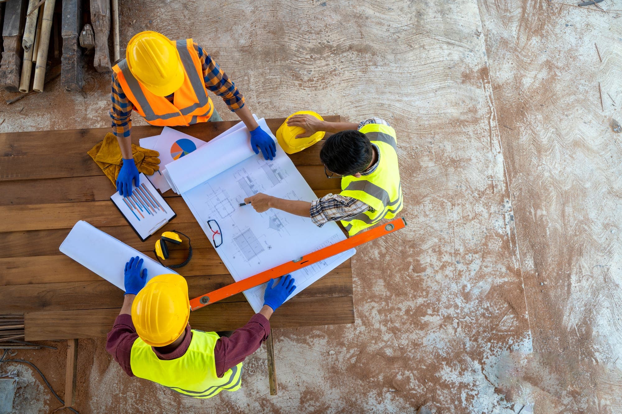 Trois compagnons en gilet et casque étudient un plan sur une table de chantier